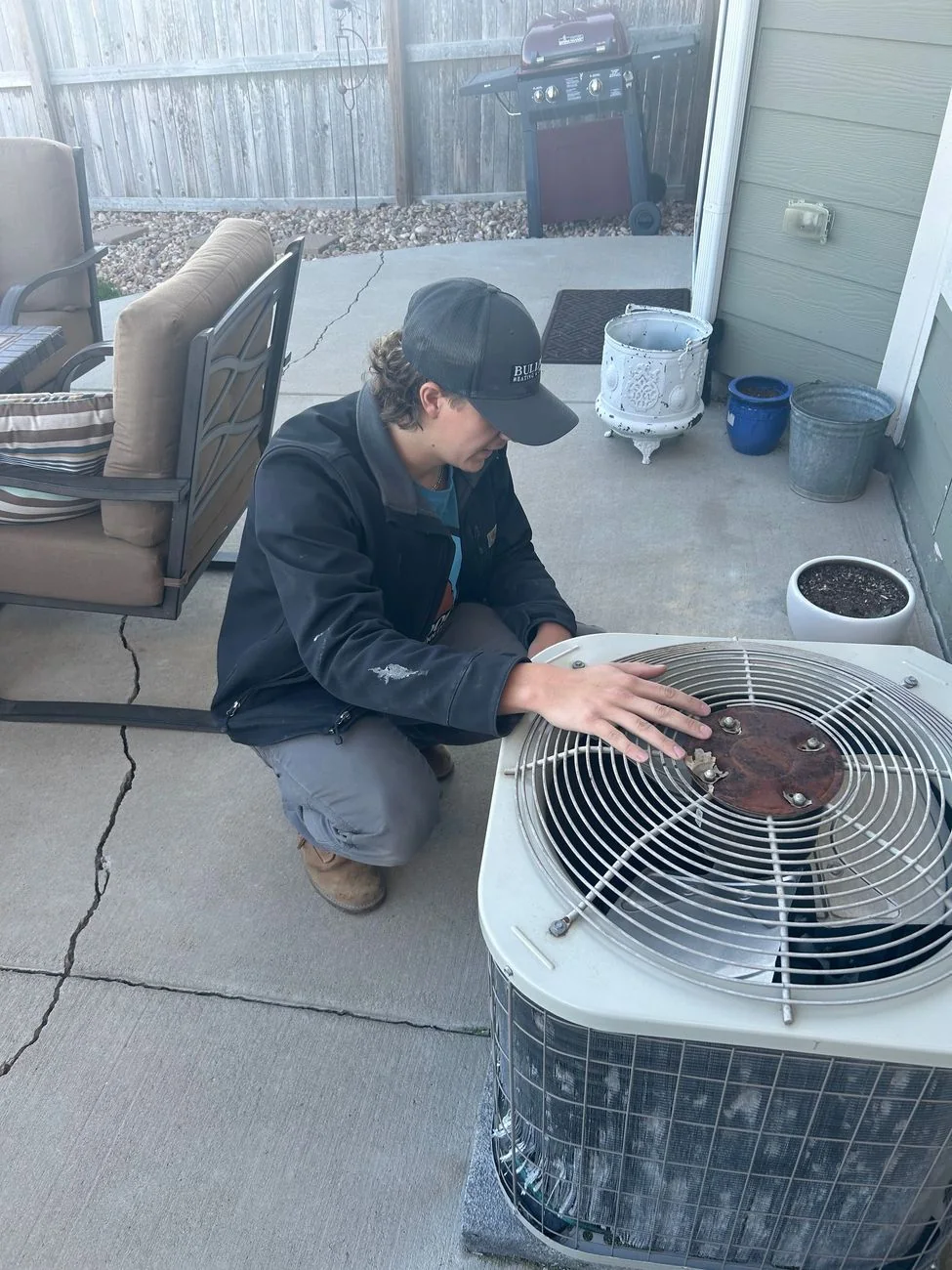 HVAC technician inspecting air conditioning unit fan in residential backyard