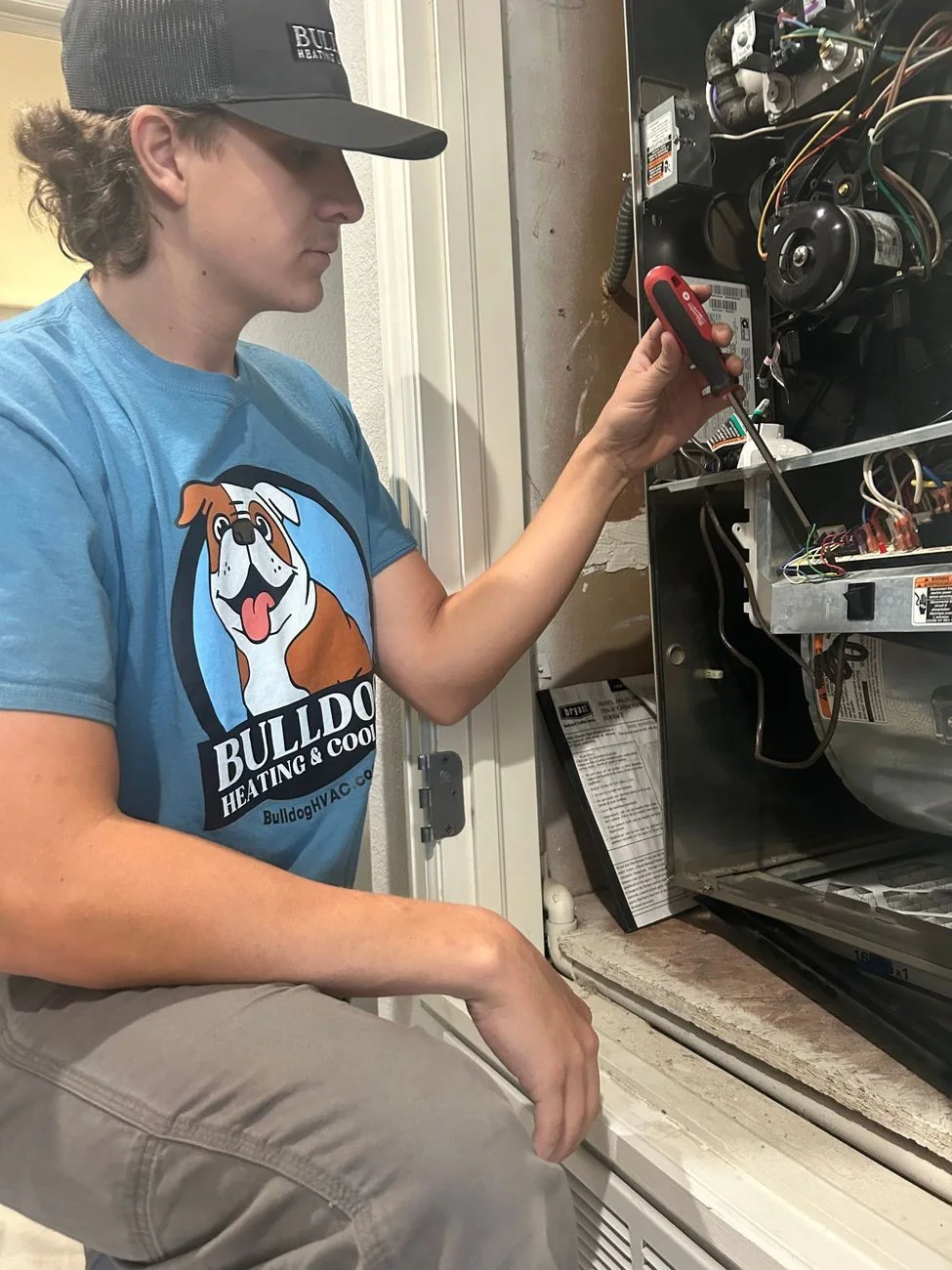 Bulldog Heating & Cooling technician servicing HVAC unit with red diagnostic tool